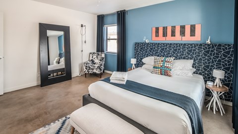 A bedroom with a large bed and a chair with a patterned cushion.
